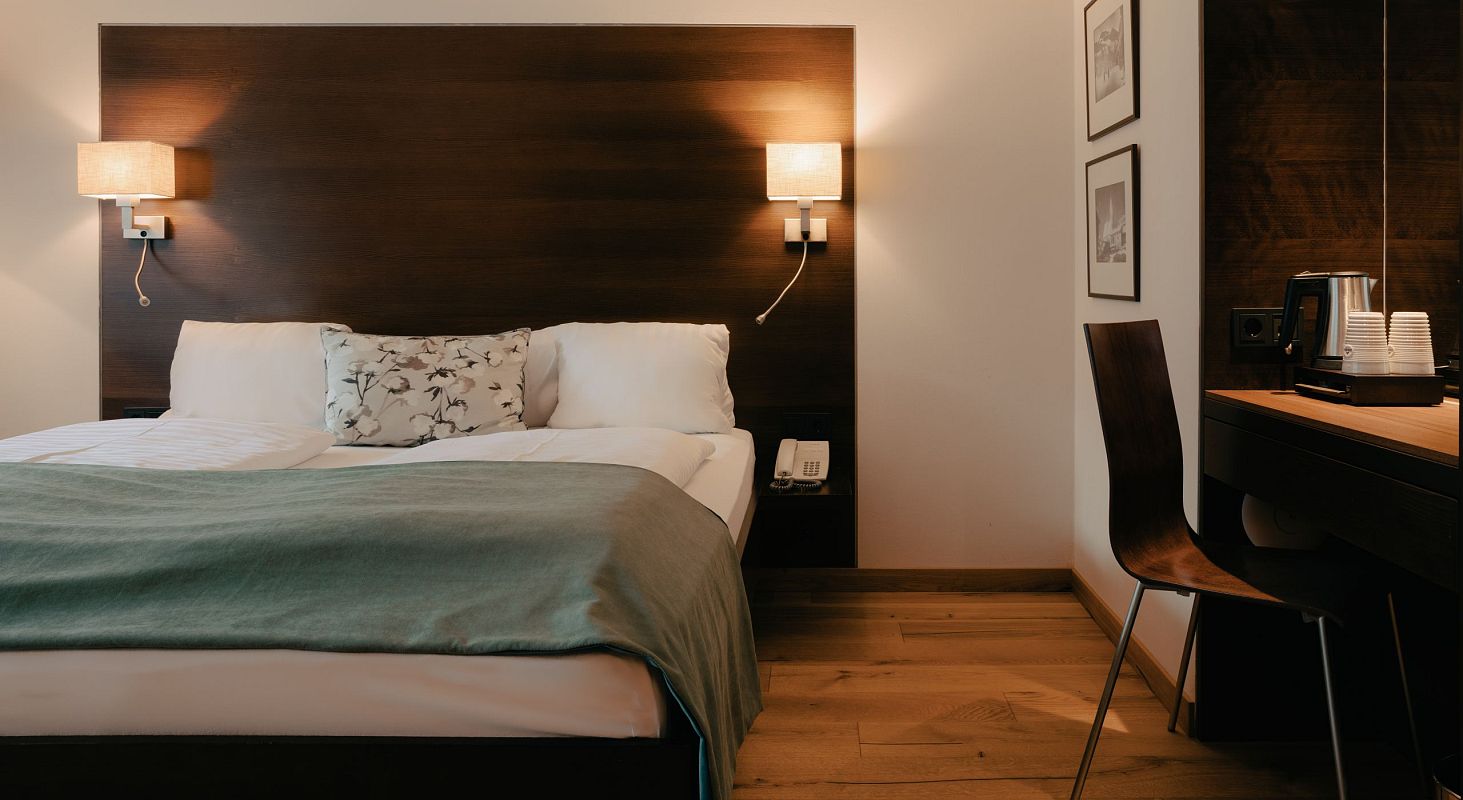 Ein Hotelzimmer mit einem großen Bett, Holzboden, Wandleuchten und einem Schreibtisch mit Stuhl, alles in stilvollem, modernem Design.