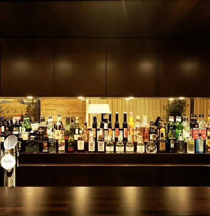 Ein elegantes Barregal mit einer Vielzahl von Spirituosenflaschen, darunter Whisky, Wodka und Liköre. Der Hintergrund ist warm beleuchtet und stilvoll gestaltet.