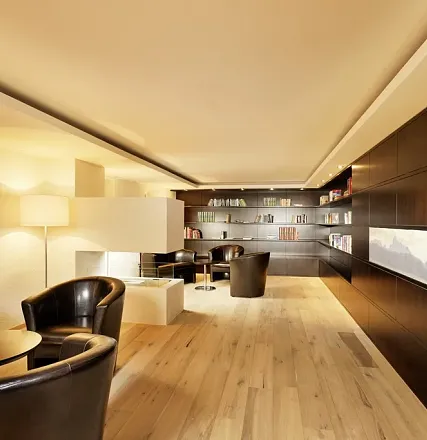 Modernes Wohnzimmer mit Holzfußboden, schwarzen Ledersesseln und eingebauten Bücherregalen. Dezente Beleuchtung und minimalistisches Design prägen den Raum.