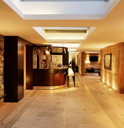 Eleganter Empfangsbereich eines Hotels mit moderner Beleuchtung, Holzwänden, einer geschwungenen Rezeption und stilvollem Dekor. Dezente Beleuchtung.