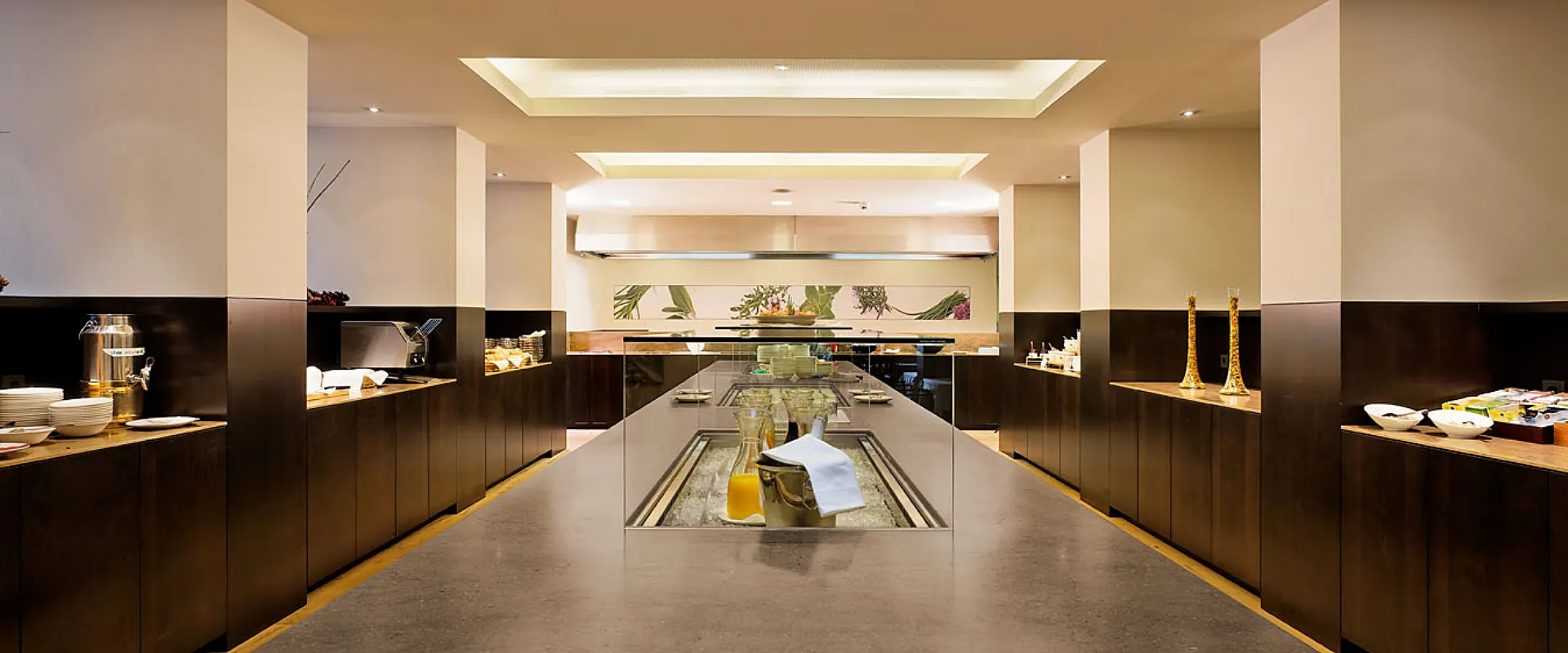 Ein moderner, eleganter Buffetbereich mit einer zentralen Insel aus dunklem Stein. Die Wände sind hell, und warme Beleuchtung schafft eine einladende Atmosphäre.