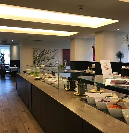 Ein elegantes Restaurant-Büfett mit einer Auswahl an Salaten, Gewürzen und Speisen. Die Einrichtung ist modern mit einem Holzfußboden und dezentem Licht.