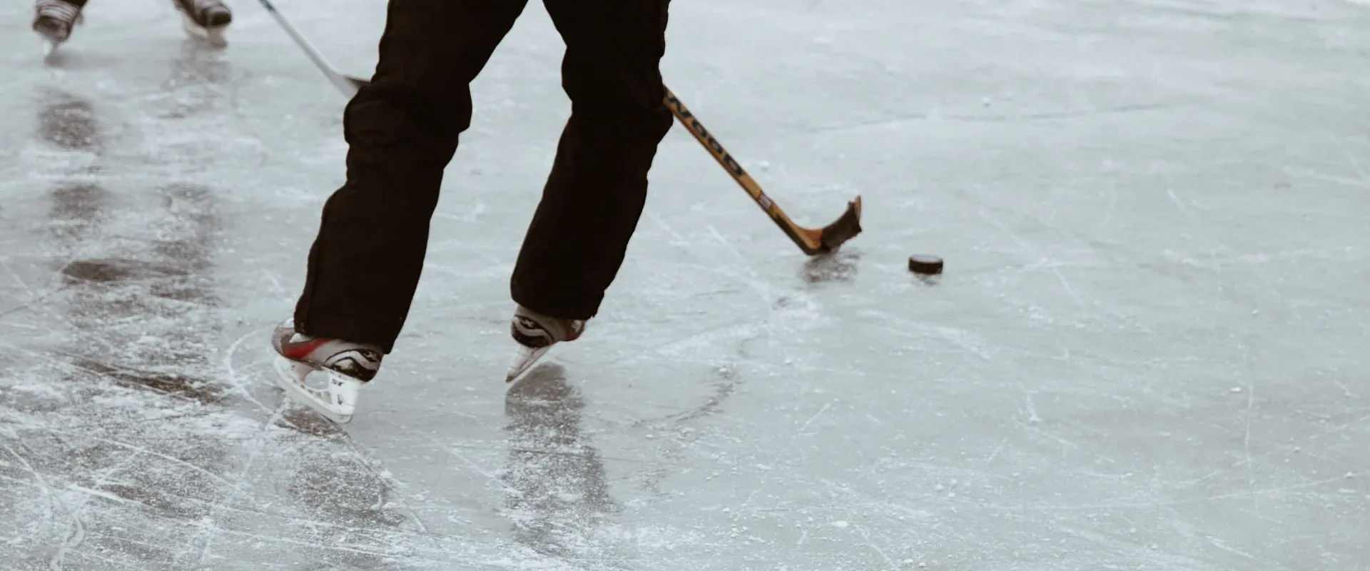Zwei Eishockeyspieler in schwarzen Uniformen spielen auf einer Eisfläche. Einer von ihnen führt den Puck mit dem Schläger. Die Umgebung ist verschwommen.