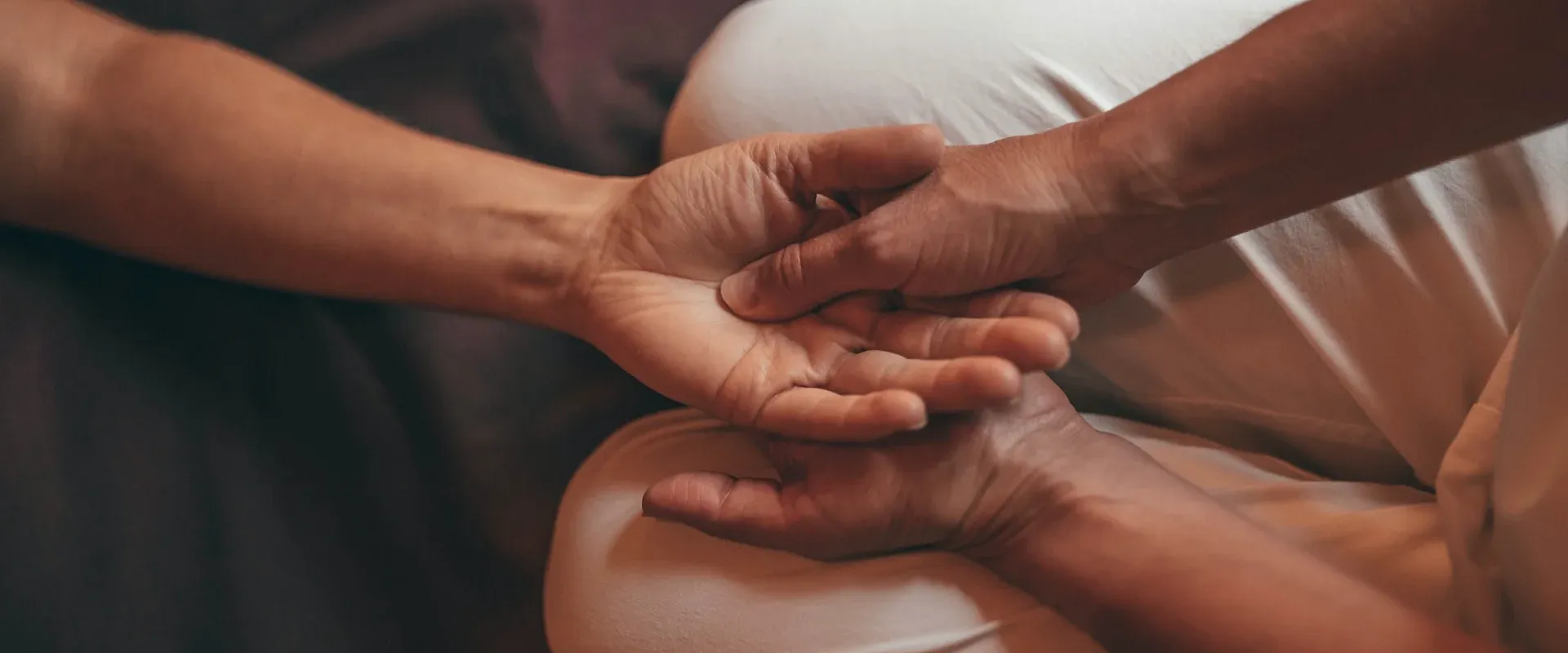 Zwei Hände, sanft ineinander gelegt, symbolisieren Vertrauen und Unterstützung. Die Szene strahlt Wärme und Fürsorglichkeit aus, vor einem dunklen Hintergrund.
