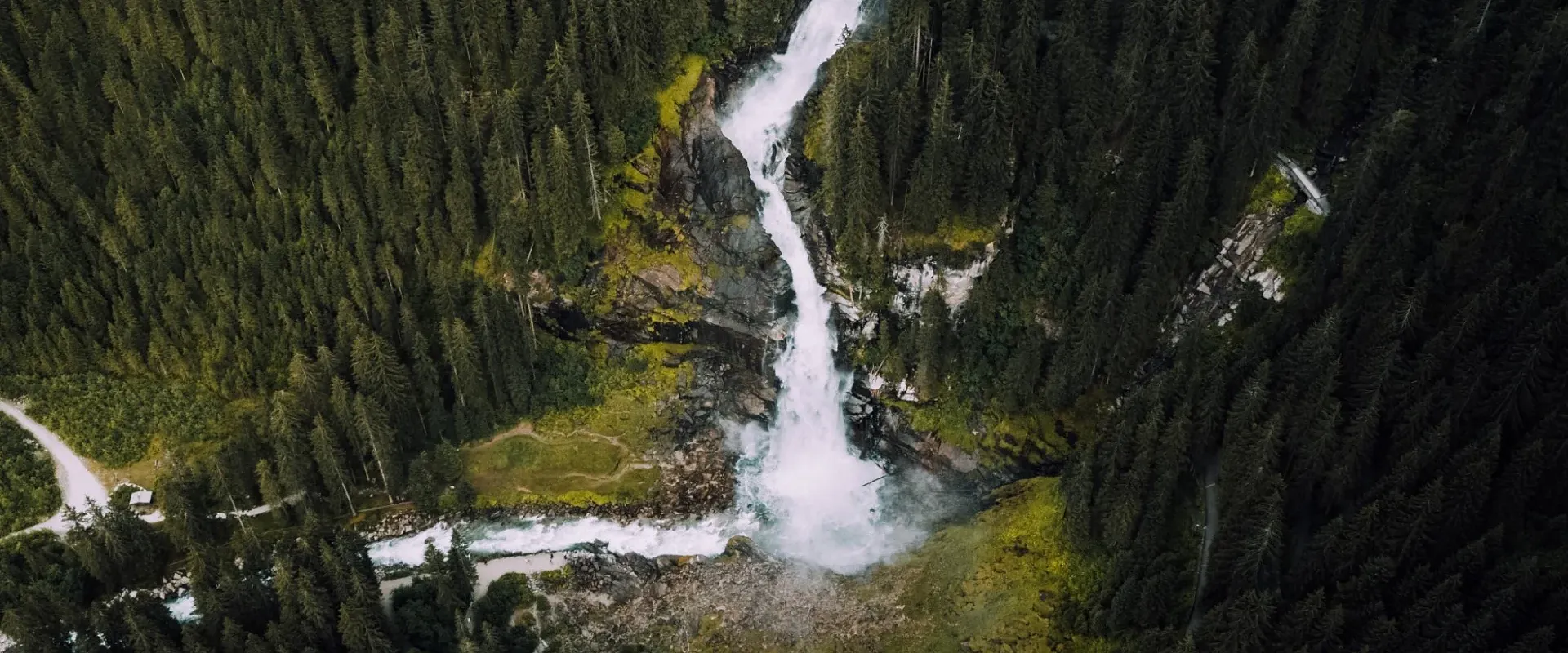 Luftaufnahme eines Wasserfalls, der sich durch einen dichten Wald schlängelt. Der Fluss teilt sich in mehrere Ströme und fließt über grüne Wiesen.
