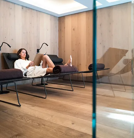 Eine Person entspannt auf einer modernen Chaiselongue in einem minimalistisch eingerichteten Raum mit Holzwänden, in bequemen Freizeitkleidung gekleidet.