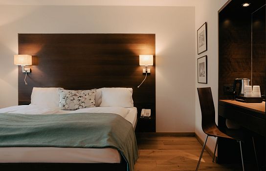 Ein Hotelzimmer mit einem großen Bett, Holzboden, Wandleuchten und einem Schreibtisch mit Stuhl, alles in stilvollem, modernem Design.