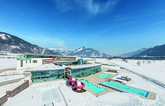 Ein modernes Gebäude mit Glasfassaden, umgeben von schneebedeckter Landschaft und Bergen. Vor dem Gebäude befinden sich mehrere Außenpools mit Dampf.