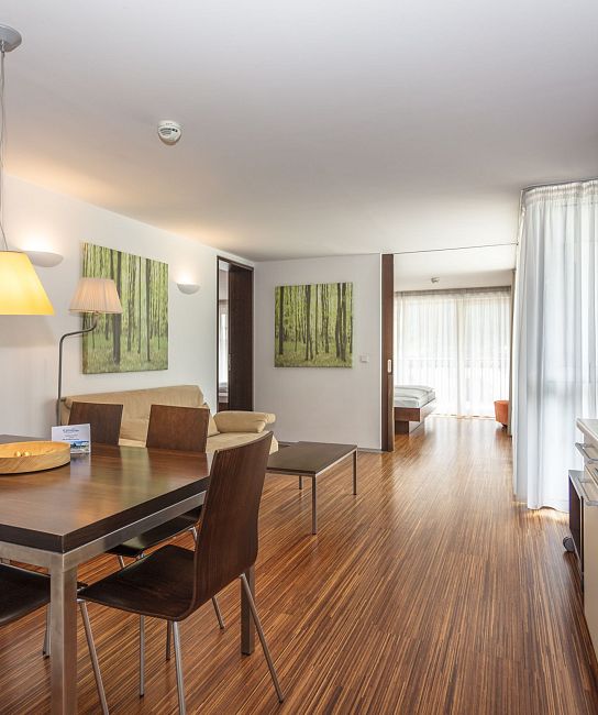 Ein modernes Apartment mit Essbereich und offener Küche, Holzböden, Kunst an den Wänden, und viel natürliches Licht. Im Hintergrund Wohnzimmer und Schlafzimmer.