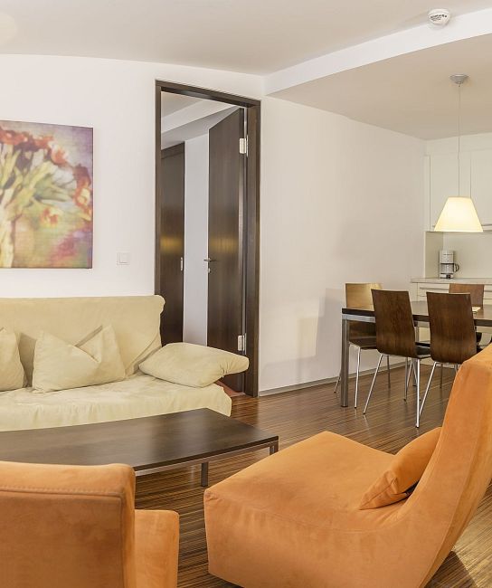 Wohnbereich mit Sofa und Sesseln, Holzboden, Esstisch vor Küchenzeile, heller Raum mit Kunst an der Wand.